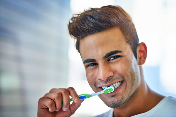 The health of my mouth depends on it. Portrait of a happy young man brushing his teeth at home. - Foto, Imagem
