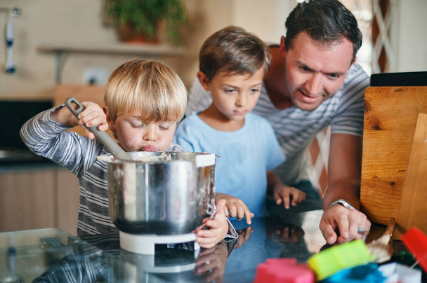 Niet alleen bakken, het is een tijd om je te binden. Schot van een jonge man bakken met zijn twee schattige zonen thuis. - Foto, afbeelding