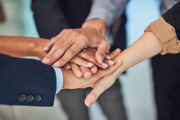 Get together and lets make this work. Closeup of a group of unrecognizable businesspeople forming a huddle with their hands while standing in the office during the day. - Photo, Image