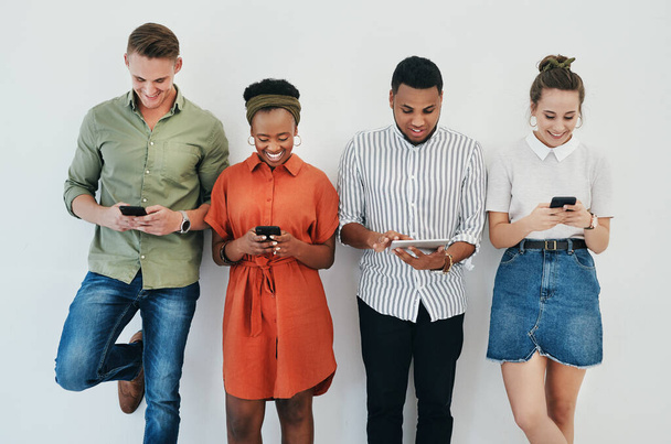 Updating our social media. Cropped shot of a diverse group of businesspeople standing against a gray background together and using technology in the office. - Foto, imagen