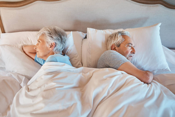 Мы все еще спорим. Обрезанный снимок несчастной пожилой пары, лежащей вдали друг от друга в постели во время разногласий дома. - Фото, изображение