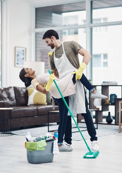 Romance changes everything. Shot of a happy young couple dancing while mopping the floor at home. - Photo, Image