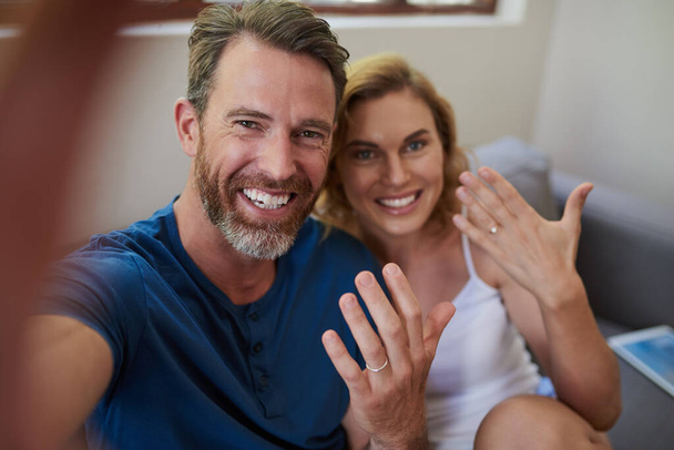 Look who just got married. Shot of a happy middle aged couple taking a selfie and showing off their wedding rings at home. - Fotografie, Obrázek
