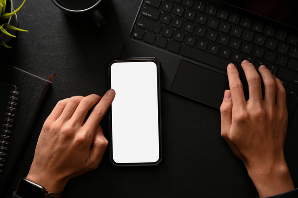 Top view, flat lay, A man using smartphone and typing on wireless tablet keyboard in black table background. Phone white screen mockup. - Photo, Image