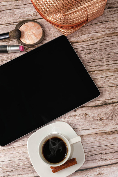 Tablet on the table surrounded by makeup bag, lipstick and coffee cup_vertical photo. - Foto, Imagen