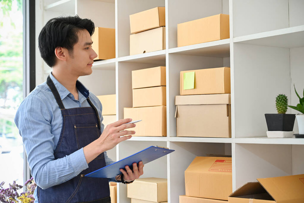 Smart Asian millennial male online business owner checking his product stock in the stock room. SME startup business entrepreneur. - Фото, зображення