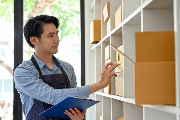 Handsome and smart Asian millennial startup businessman, online store shop owner, working in his store and checking the parcel boxes. - Photo, Image