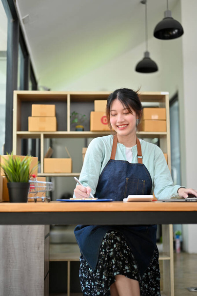 Portrait, Attractive Asian young woman, online store owner, working at her desk, doing a sales accounts report. Small online business. - Фото, зображення