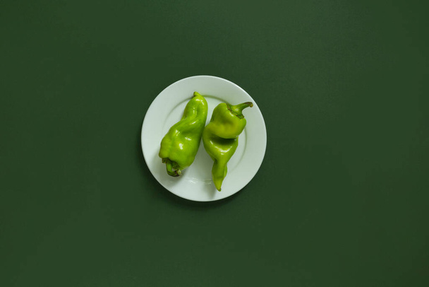 Πράσινες πιπεριές σε λευκό πιάτο στο πράσινο φόντο. - Φωτογραφία, εικόνα