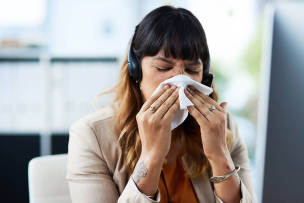 Ik denk dat ik verkouden ben. Gehakt schot van een aantrekkelijke jonge zakenvrouw die lijdt aan een verkoudheid en snuit haar neus terwijl in haar kantoor. - Foto, afbeelding