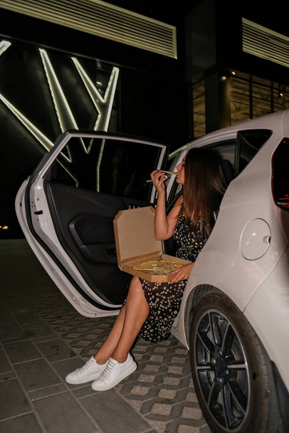 A conviver. Jovem mulher casualmente em um estacionamento comendo pizza à noite. Estilo de vida geração gen z milenar - Foto, Imagem