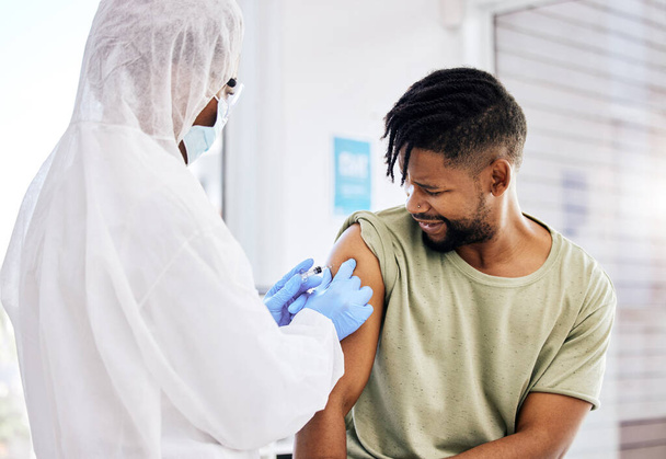 A jab is all it takes. Cropped shot of an unrecognizable doctor administering the covid 19 vaccine to a handsome young male patient. - Φωτογραφία, εικόνα