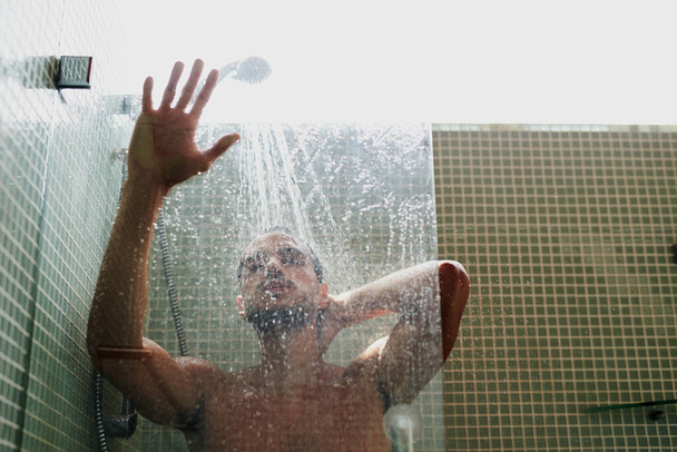 La ducha es un gran lugar para refrescarse. Cortado tiro de un joven guapo teniendo una ducha refrescante en casa. - Foto, imagen