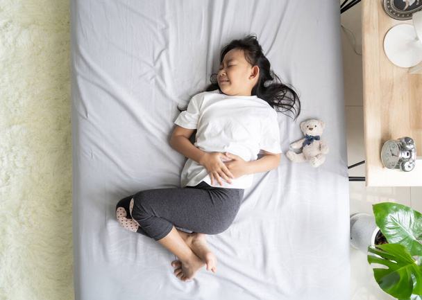 Top view Ασιατικό κοριτσάκι στο κρεβάτι της έχει στομαχόπονο, υγιή ιδέα έννοια - Φωτογραφία, εικόνα