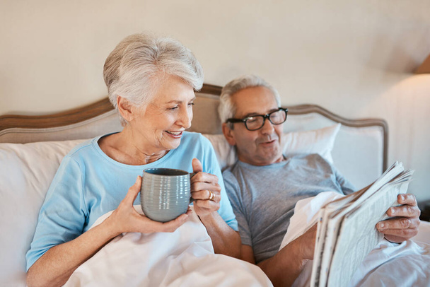 We still like the good old fashioned newspaper. Cropped shot of a senior man reading a newspaper in bed while his wife drinks a cup of coffee. - Photo, image