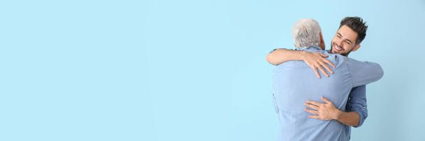 Happy young man hugging his father on light blue background with space for text - Foto, afbeelding