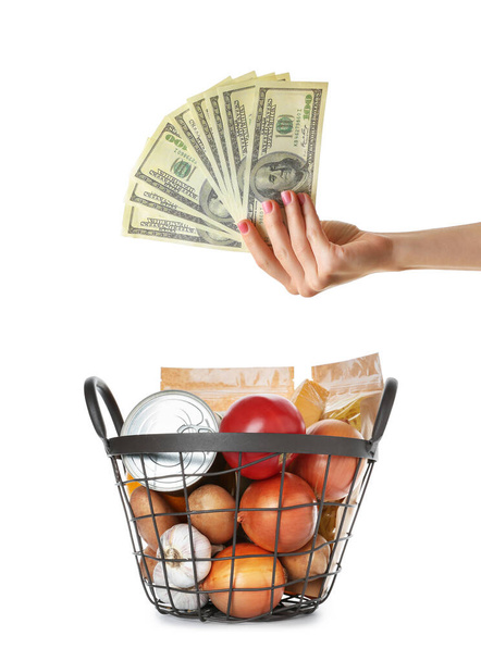 Shopping basket with products and hand holding money on white background. Food price increase - Foto, afbeelding
