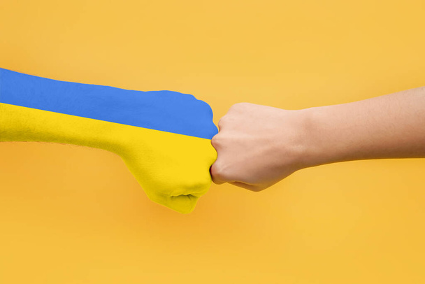 Hand in colors of Ukrainian flag and hand of young woman bumping fists on yellow background - Photo, Image