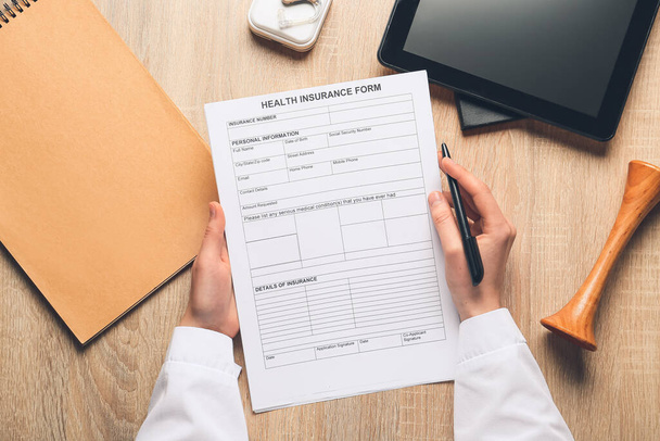 Female doctor holding health insurance form on wooden background - Photo, image