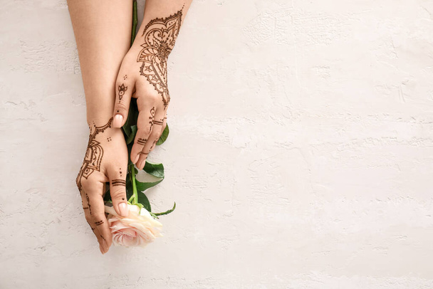 Female hands with beautiful henna tattoo and rose flower on light background, closeup - Foto, afbeelding