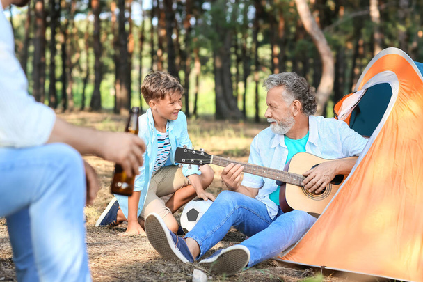 Ανώτερος άνθρωπος παίζει κιθάρα για την οικογένειά του στο δάσος - Φωτογραφία, εικόνα