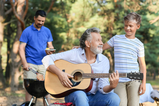 Старший чоловік грає на гітарі для свого маленького онука на вечірці барбекю в літній день
 - Фото, зображення
