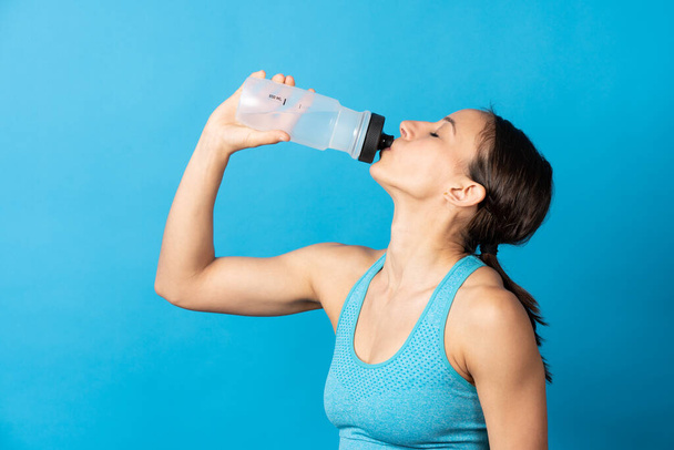 Hispanic fit woman drinking water isolated on blue background. Hidration after sport concept - Foto, afbeelding