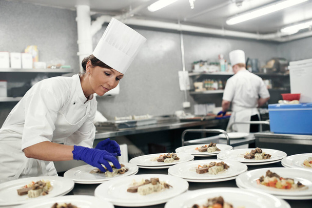 Превратить ужин в шедевр. Снимок шеф-повара, покрывающего еду для обслуживания еды на профессиональной кухне. - Фото, изображение