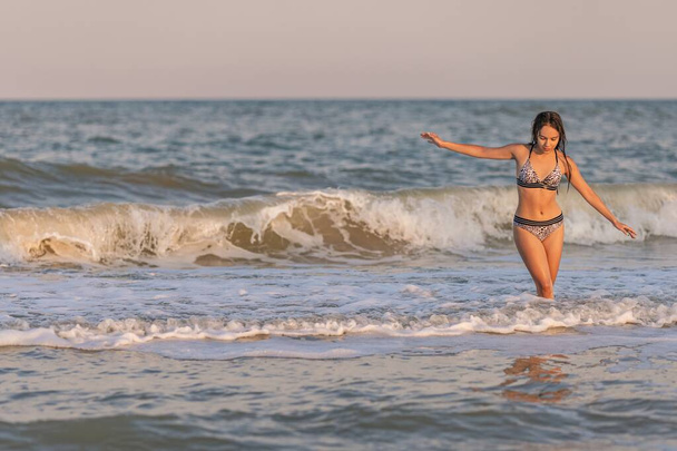 A girl with loose hair walks on the sea with waves and enjoys the sun - Fotoğraf, Görsel