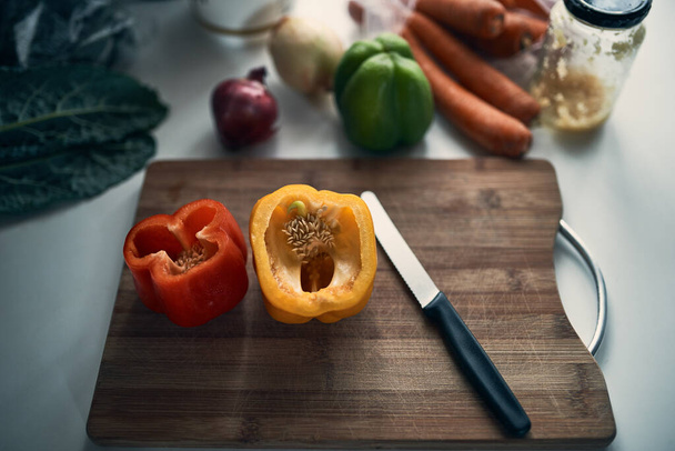 Βασικά συστατικά. Υψηλής γωνίας βολή ψιλοκομμένες πιπεριές σε ένα ξύλο κοπής surround από διάφορα λαχανικά σε έναν πάγκο κουζίνας. - Φωτογραφία, εικόνα