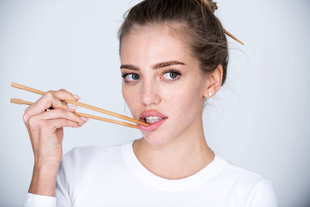 Chopsticks near sexy lips mouth. Pretty girl picking lips with chopsticks. Sexy mouth for sushi advertising. Concept of chinese or japanese food. - Foto, afbeelding