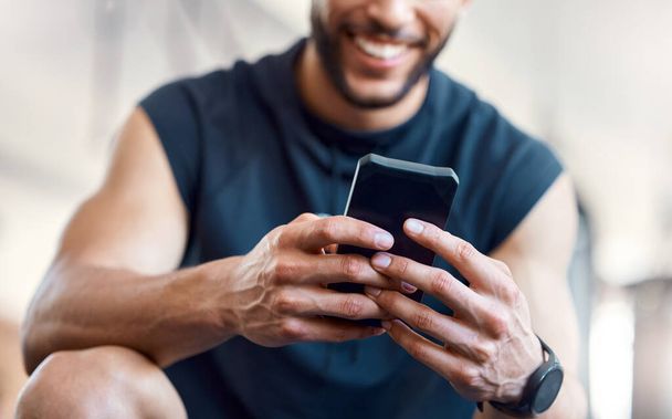 Download the best workout apps today. Low angle shot of an unrecognisable man using a cellphone in a gym. - Foto, afbeelding