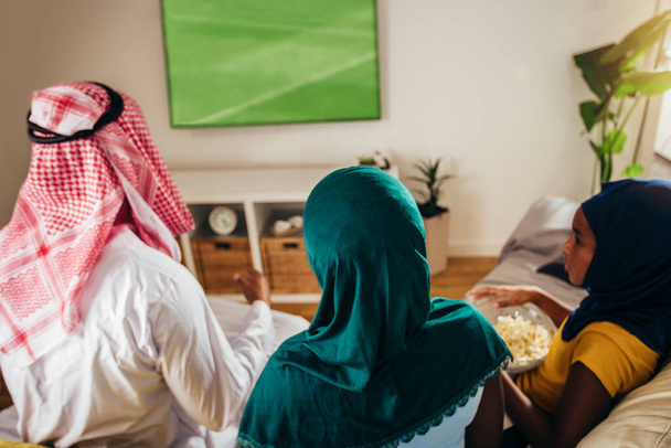 Hombre árabe mirando la televisión en casa durante un evento deportivo con su familia. Ver el fútbol juego. - Foto, Imagen