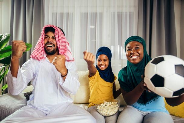 Arab ogląda telewizję w domu podczas imprezy sportowej z rodziną. Oglądanie piłki nożnej gry. - Zdjęcie, obraz