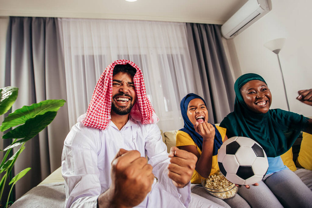 Arab man looking TV at home during a sport event with his family. Watching football game. - Photo, Image