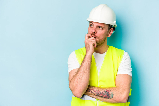 Young laborer caucasian man isolated on blue background relaxed thinking about something looking at a copy space. - Photo, Image