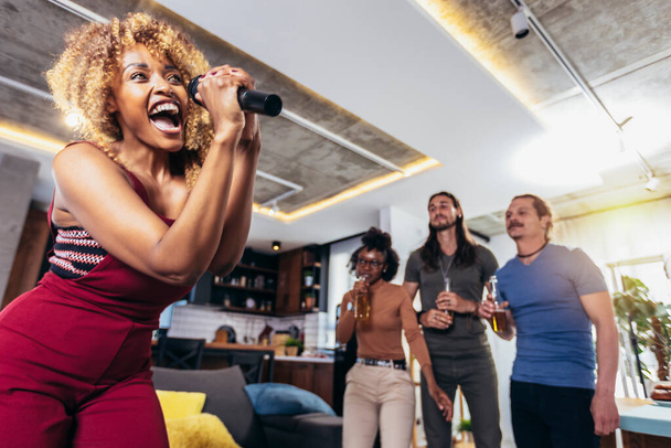 Group of young multicultural friends having party singing song using microphone at home. - Foto, Bild