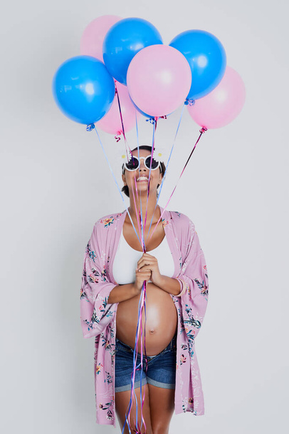 Dziewczynka, chłopiec różowy czy niebieski jakie będzie moje dziecko. Studio zdjęcie pięknej młodej kobiety w ciąży trzymającej niebiesko-różowe balony na szarym tle. - Zdjęcie, obraz