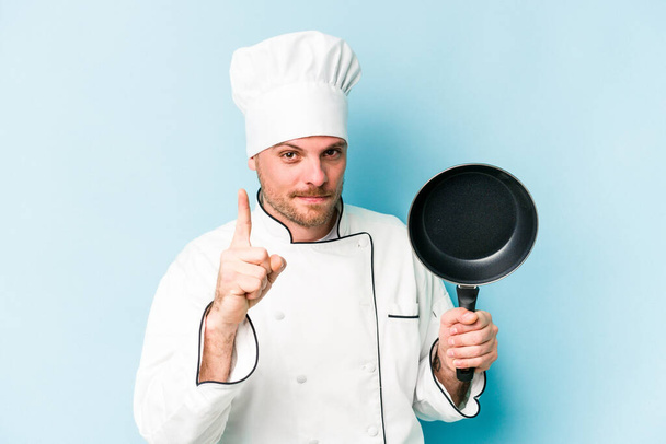 Young caucasian chef man holding flying pan isolated on blue background having an idea, inspiration concept. - Φωτογραφία, εικόνα