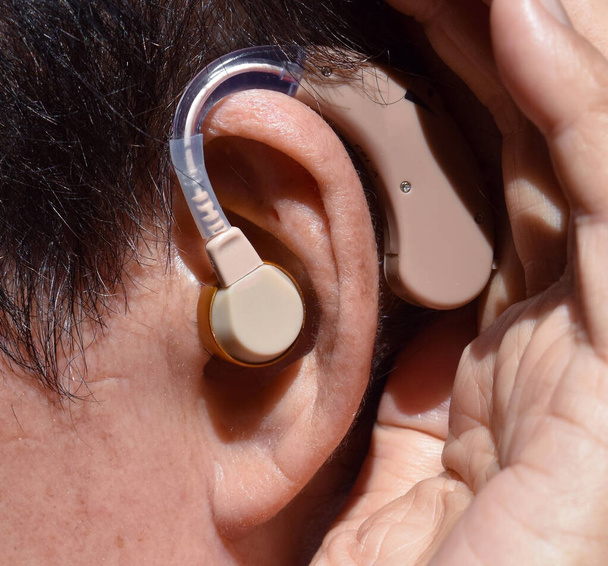 Электронный слуховой аппарат в ухо азиатского старика с полной глухотой. - Фото, изображение