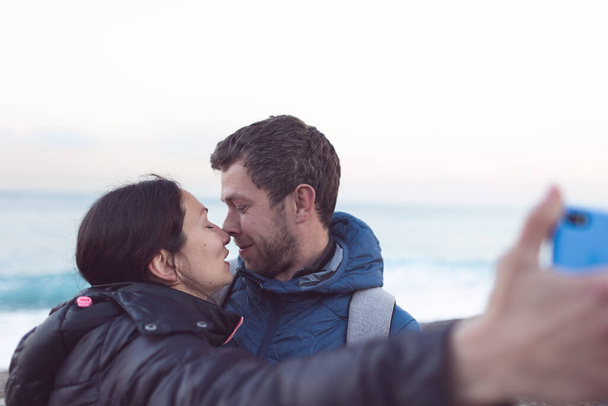 Egy férfi és egy nő csókolózik a parton, szerelmesek szelfit készítenek a tenger közelében, két ember ölelkezik. - Fotó, kép
