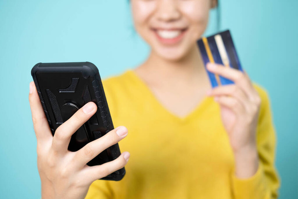 Nuori nainen ottaa kuvan itsestään käyttämällä älypuhelinta ja luottokorttia maksamaan verkossa. - Valokuva, kuva