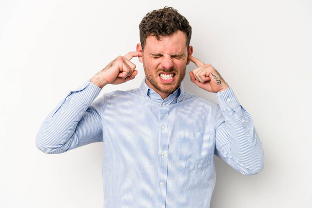 Young caucasian man isolated on white background covering ears with fingers, stressed and desperate by a loudly ambient. - Photo, Image