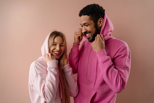 Fashion studio portrait of a happy young couple in hoodie posing over pink background. - Foto, Imagen