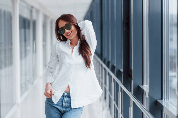 Brunette in white shirt that walks indoors in modern airport or hallway at daytime. - Foto, Bild
