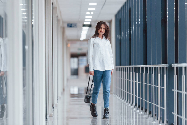 Brunette in white shirt walks indoors in modern airport or hallway at daytime. - Foto, imagen