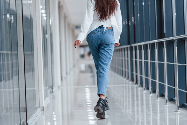 Vista posteriore della ragazza in camicia bianca che cammina all'interno in aeroporto moderno o corridoio durante il giorno. - Foto, immagini