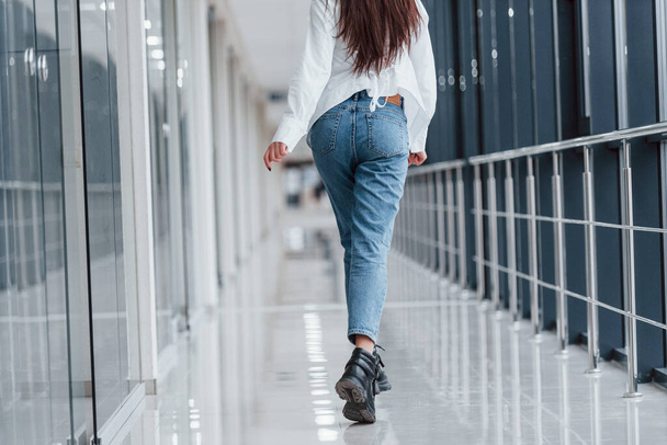 Rear view of brunette in white shirt that walks indoors in modern airport or hallway at daytime. - Φωτογραφία, εικόνα