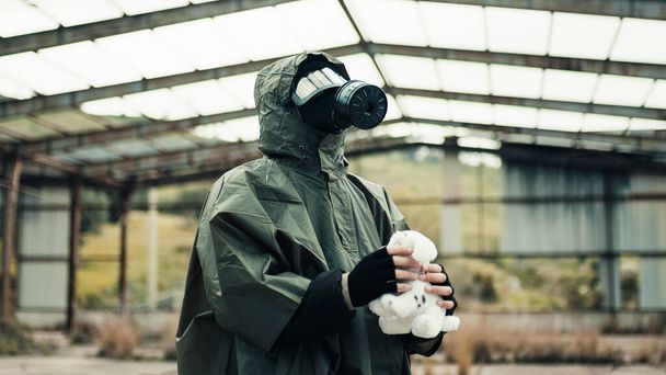 Ένας άντρας με μάσκα αερίου βρίσκει ένα λούτρινο ζωάκι σε ένα νοσοκομείο σε πόλεμο. - Φωτογραφία, εικόνα