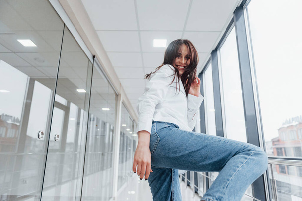 Close up view of brunette in white shirt indoors in modern airport or hallway at daytime that making kick with leg. - Valokuva, kuva